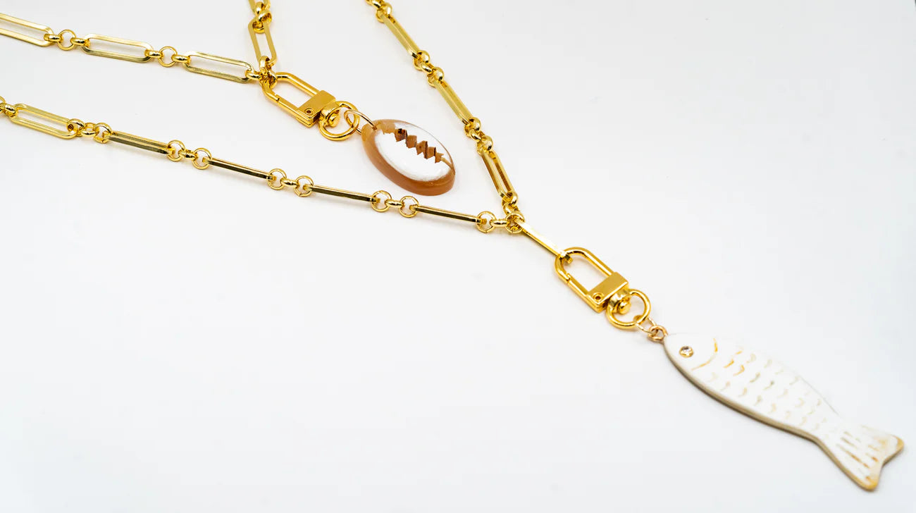 Akola cowrie charm layered with fish charm on a puka strand