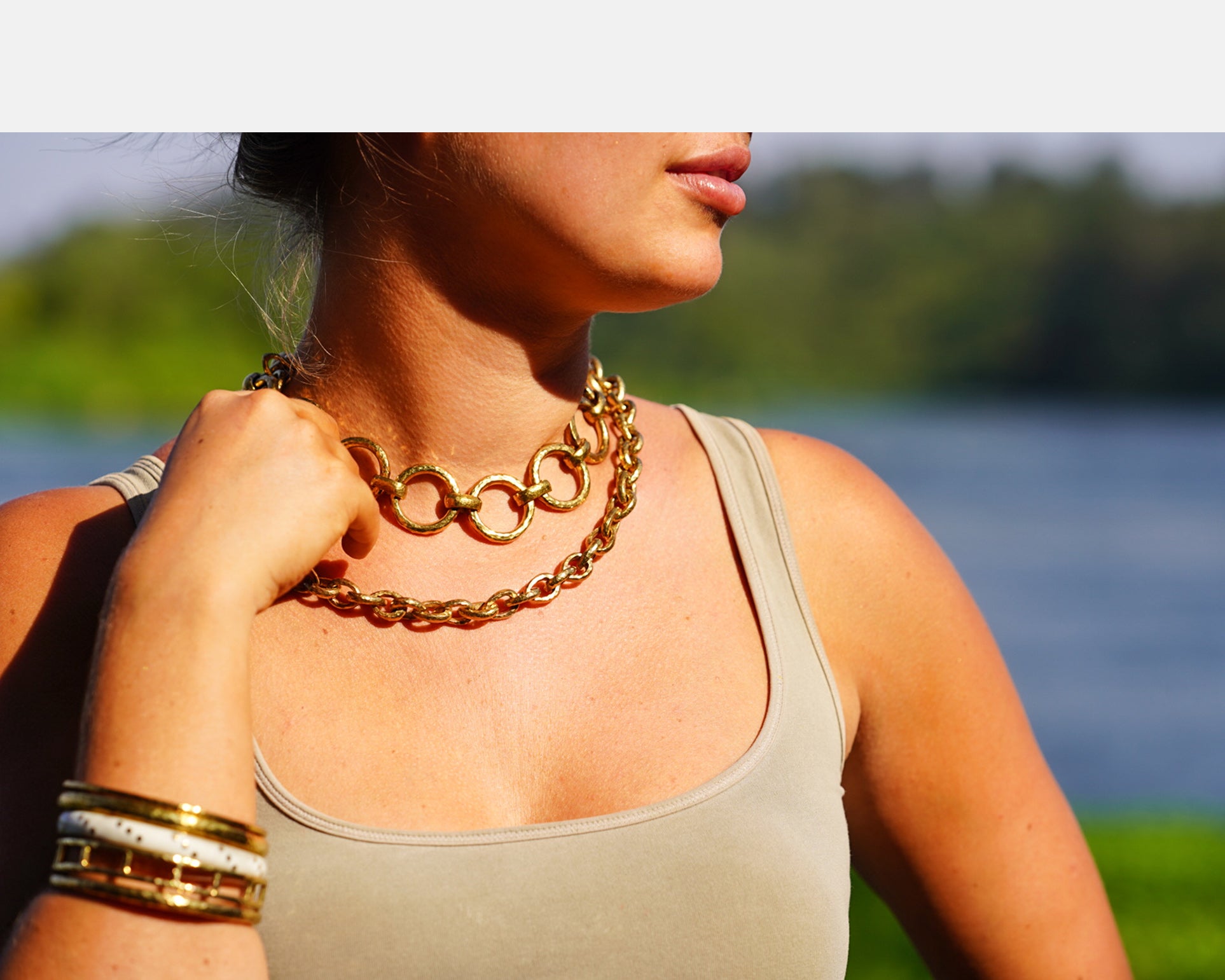 Woman wearing a hammered brass chain necklace with a blurred natural background